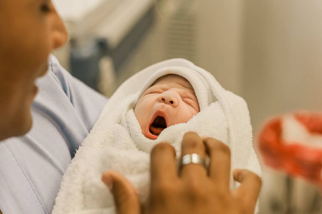 postpartum doula holding a newborn baby who is swaddled and yawning.